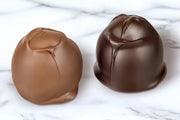 Two chocolate covered cherry cordials made by Morkes chocolates set on white marble table. 