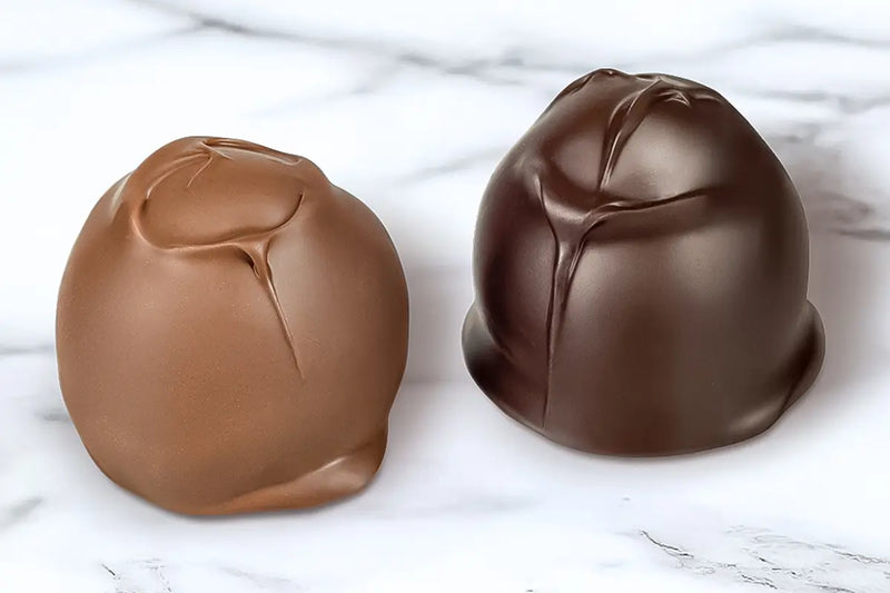 Two chocolate covered cherry cordials made by Morkes chocolates set on white marble table. 