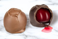 Two chocolate covered cherry cordials made by Morkes chocolates. One cherry cordial is cut open with syrup flowing out. 