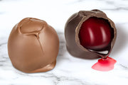 Two chocolate covered cherry cordials made by Morkes chocolates. One cherry cordial is cut open with syrup flowing out. 