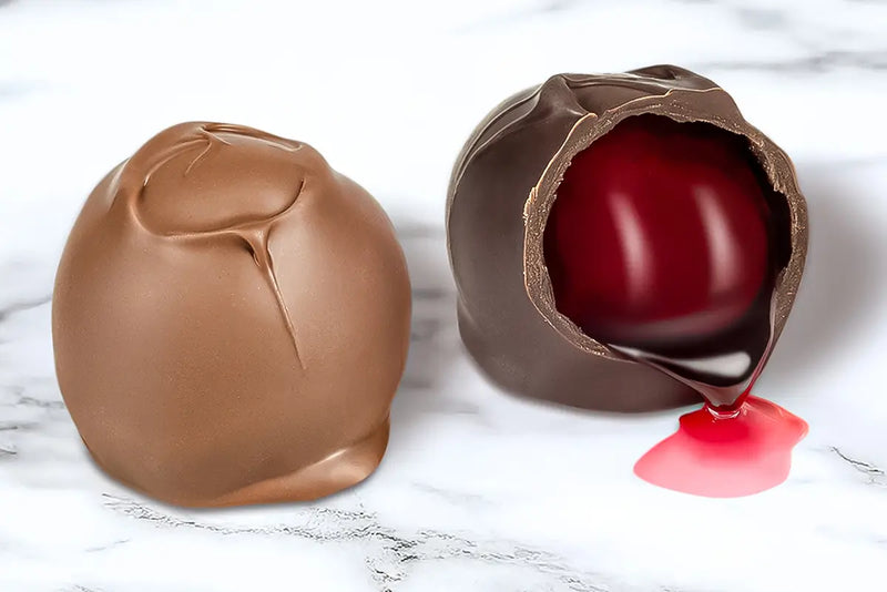 Two chocolate covered cherry cordials made by Morkes chocolates. One cherry cordial is cut open with syrup flowing out. 