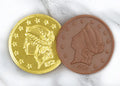 A closeup picture of two Chocolate Gold Coins by Morkes Chocolates placed on a marble floor. One of the coins is unwrapped