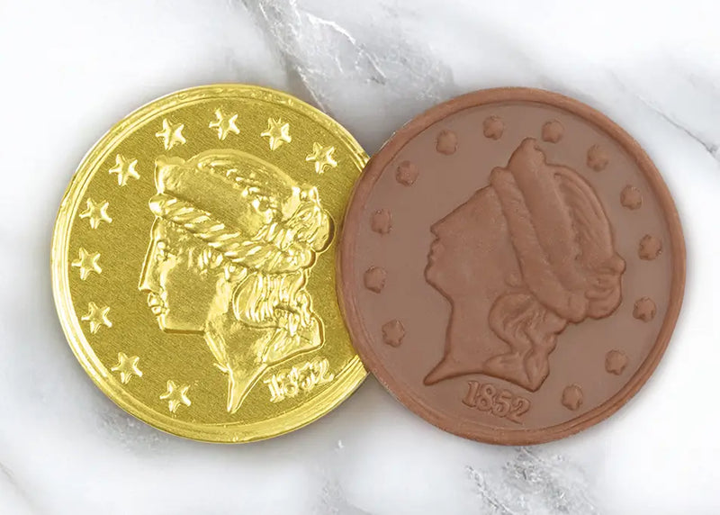 A closeup picture of two Chocolate Gold Coins by Morkes Chocolates placed on a marble floor. One of the coins is unwrapped