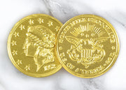 A closeup picture of two Chocolate Gold Coins by Morkes Chocolates placed on a marble floor.