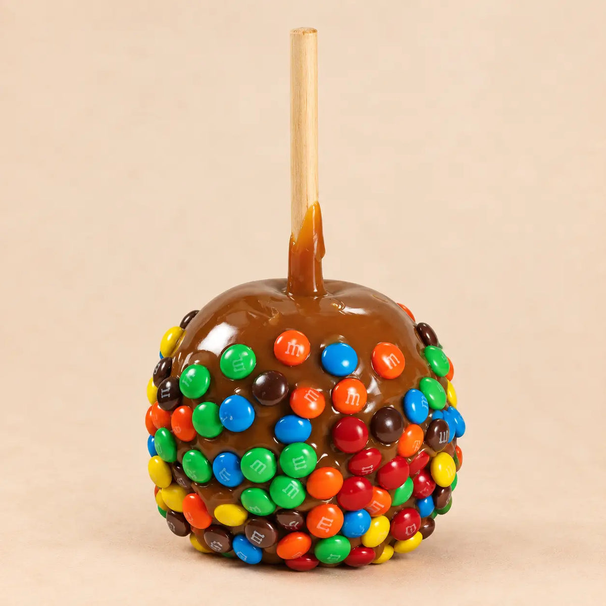 A caramel apple coated in glossy caramel and covered with colorful mini M&M's.