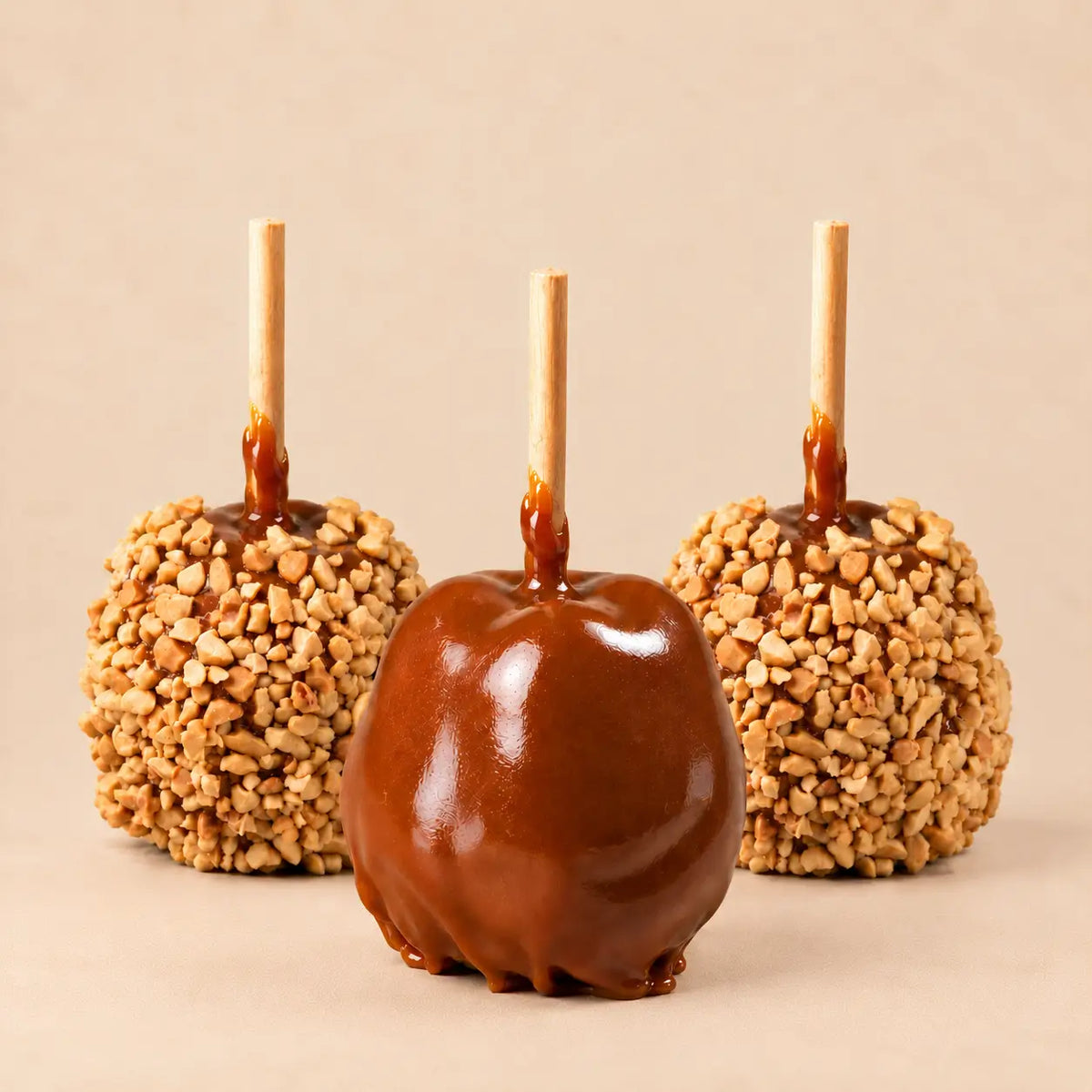 Three Morkes caramel apples placed on a warm beige background. The front apple is a plain caramel apple, and the two behind are peanut caramel apples.