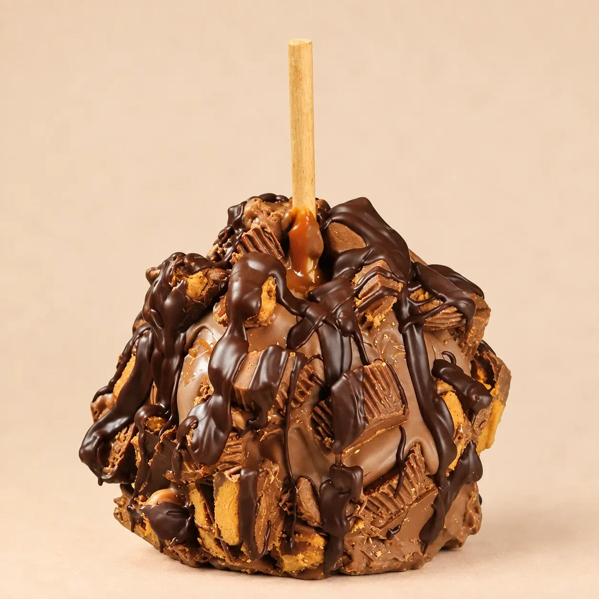 A gourmet caramel apple with multiple layers of chocolate and peanut butter toppings, set against a beige background.