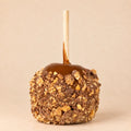A single caramel apple with a wooden stick, coated in glossy caramel and topped with Snickers crumb.