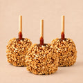 Three peanut caramel apples from Morkes Chocolates, placed on a warm beige background. 