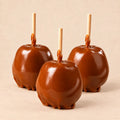 Three plain caramel apples from Morkes Chocolates, placed on a warm beige background. 