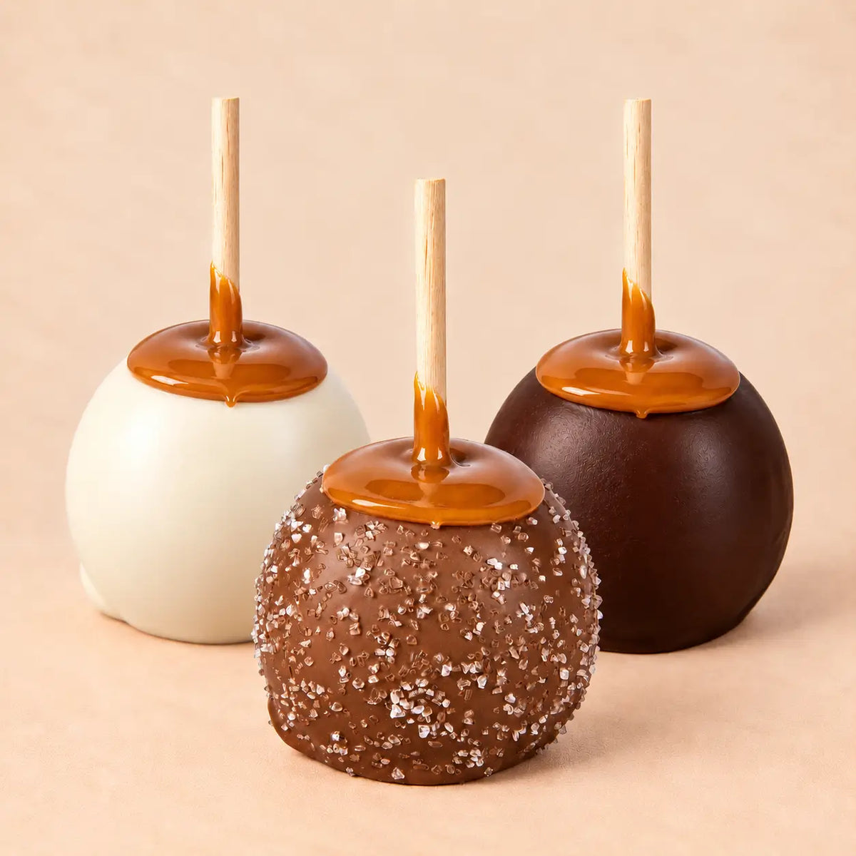 A trio of chocolate caramel apples from Morkes Chocolates. In the front, there is a milk chocolate caramel apple covered with sea salt. In the back, there is a white chocolate caramel apple on the left and a dark chocolate caramel apple on the right.