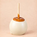 A white chocolate caramel apple from Morkes Chocolate set on a warm beige background